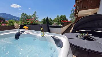 A hot tub with a view of mountains, surrounded by outdoor furniture and flowers.