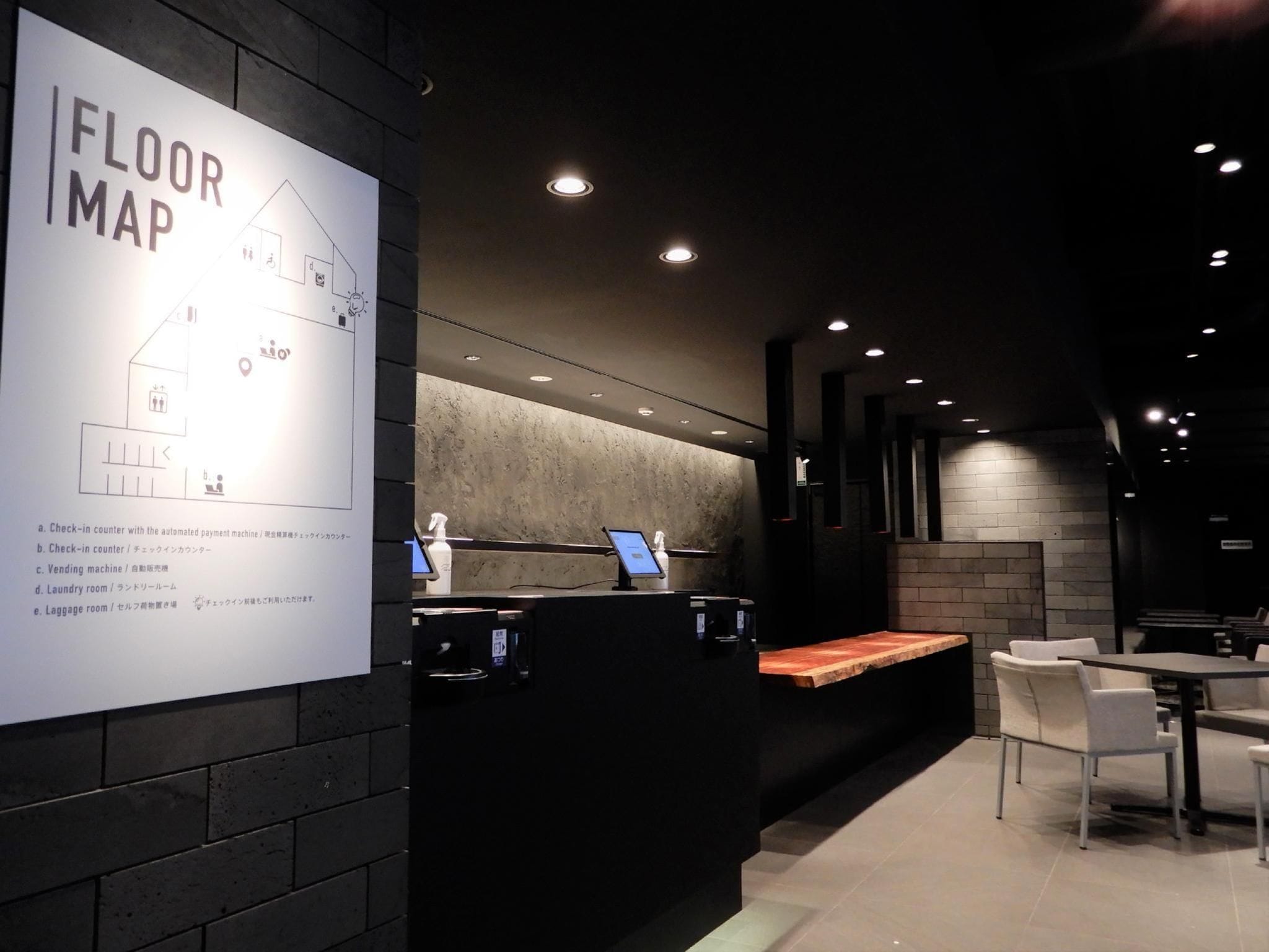 A hotel reception area with a floor map, check-in counters, a vending machine, and a seating area.