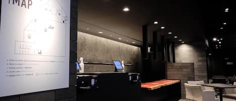 A hotel reception area with a floor map, check-in counters, a vending machine, and a seating area.