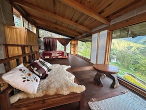 Un intérieur en bois comprenant un lit, des oreillers, une petite table et de grandes fenêtres donnant sur un paysage montagneux.