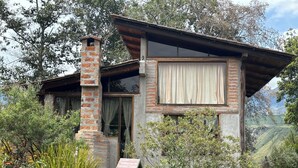 A rustic house with a brick chimney, large windows, and a view of the surrounding hills. - Island in the Sky--Shisa House
Small custom home built with love in Cahuasqui (Cahuasqui)