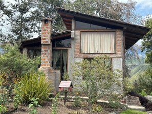A rustic house with a brick chimney, large windows, and a view of the surrounding hills.