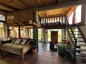 A rustic interior with a loft bed, a wooden staircase, and a large window.