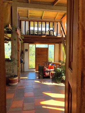A rustic interior with a wooden staircase, a view of the outdoors, and a seating area with a table.