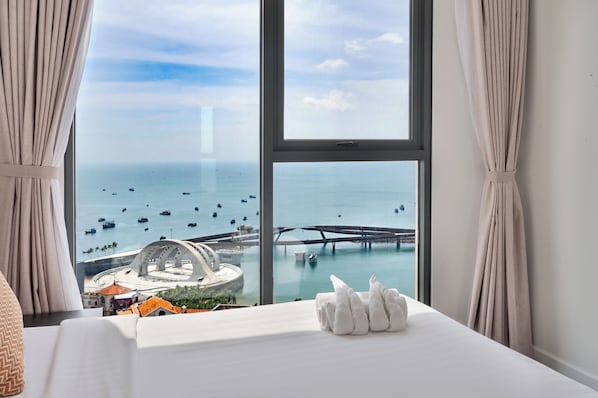 Ein Hotelzimmer mit großem Fenster und Blick auf das Meer, Boote und eine Brücke.