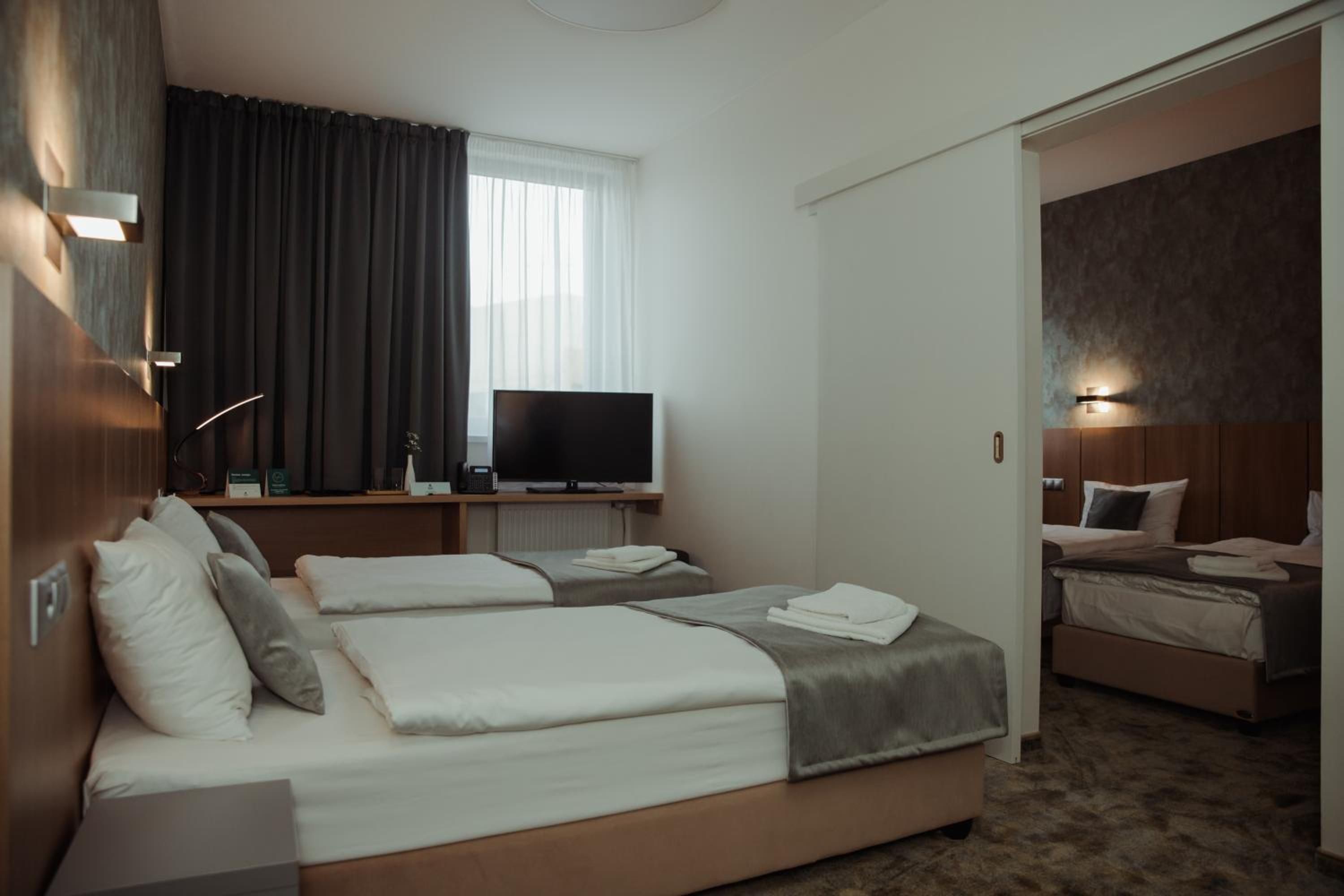 Una habitación de hotel con una cama, televisor, escritorio con lámpara y ventana con cortinas.
