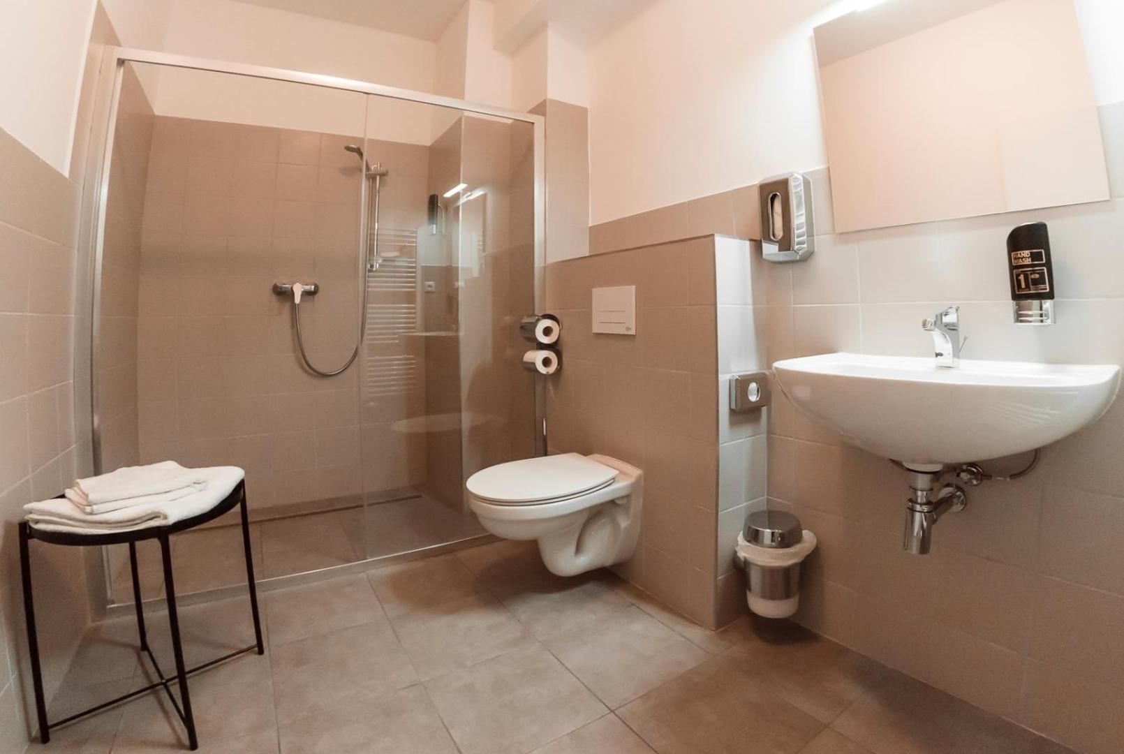 Un baño moderno con ducha de vidrio, inodoro, lavamanos y un pequeño cubo de basura.