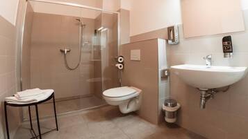 Un baño moderno con ducha de vidrio, inodoro, lavamanos y un pequeño cubo de basura.