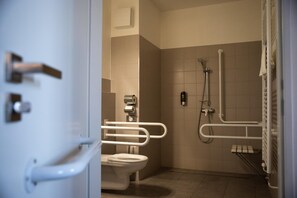 A bathroom with a toilet, a shower, and a handrail. - Hotel Arena (Kosice)