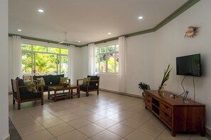 A spacious living room with a sofa set, a coffee table, a TV on the wall, and a ceiling fan. - 340 Degrees Mountain View Apartments (Mahé Island)