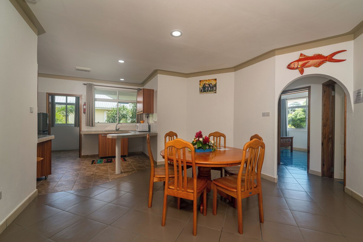 A modern kitchen with a dining area, wooden chairs, and a fish artwork on the wall.