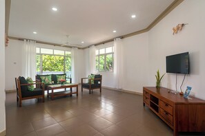 A spacious living room with a flat-screen TV, wooden furniture, and large windows. - 340 Degrees Mountain View Apartments (Mahé Island)