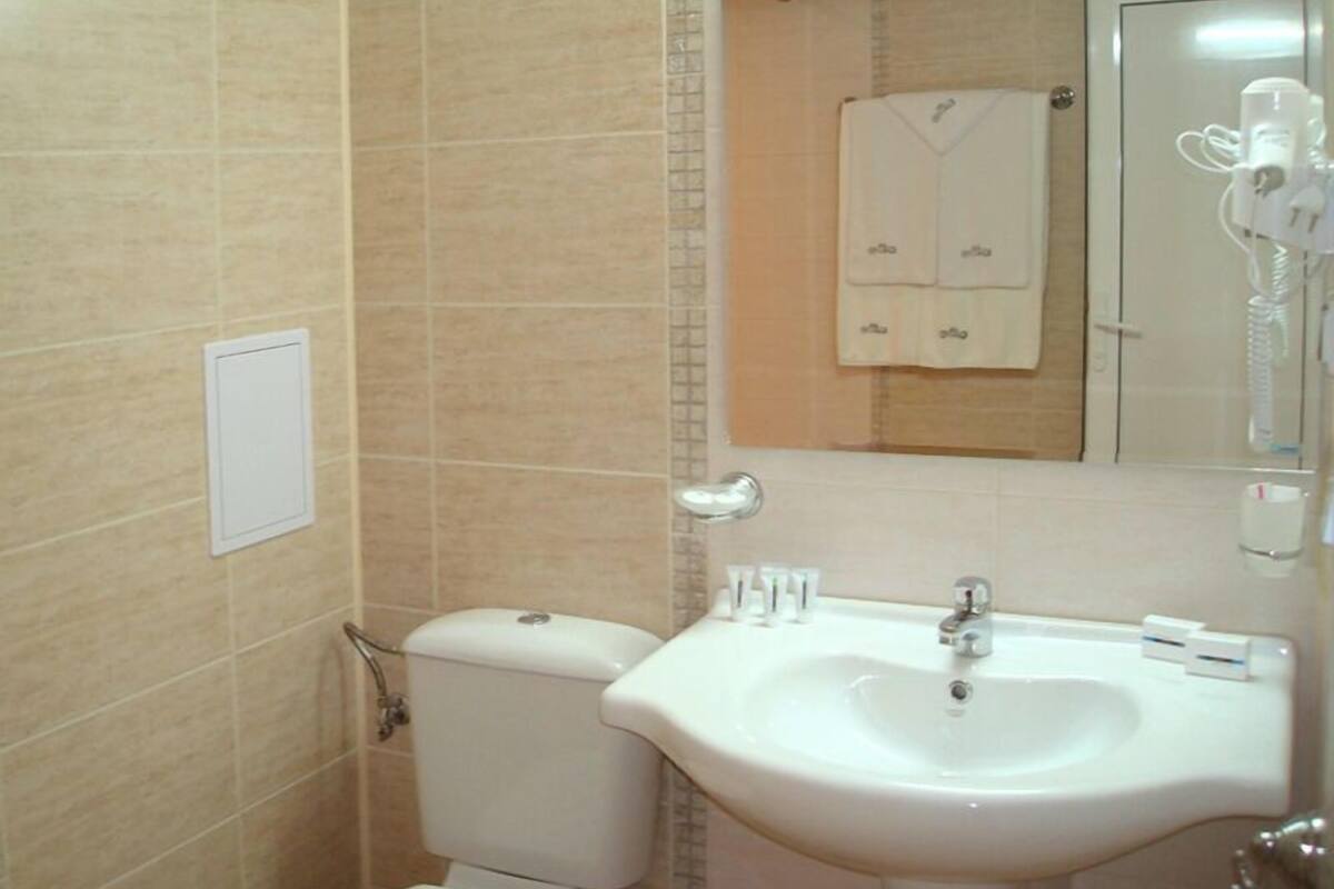 Un baño con inodoro, lavabo, espejo, toallero y una toalla colgada en la pared.