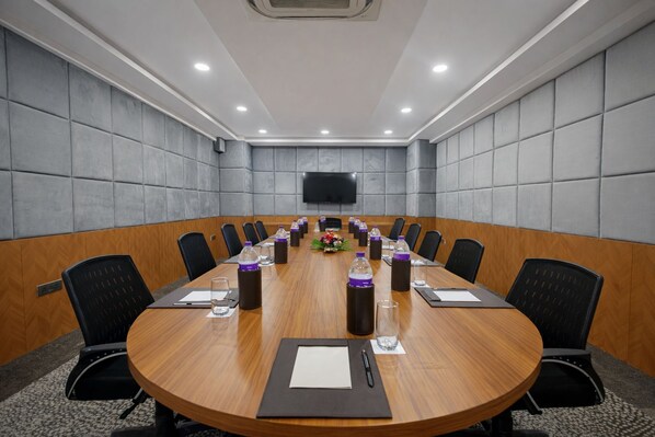 A conference room with a long table, chairs, water bottles, and a flat-screen TV on the wall. - Saaz Hotel Indore (Indore)