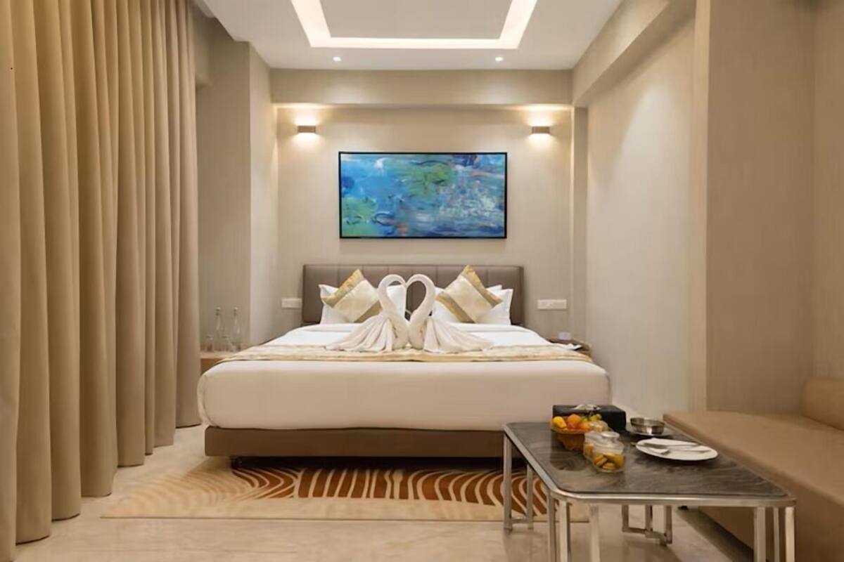 Habitació d'hotel amb llit, un quadre a la paret, taula amb articles per esmorzar i un sofà.