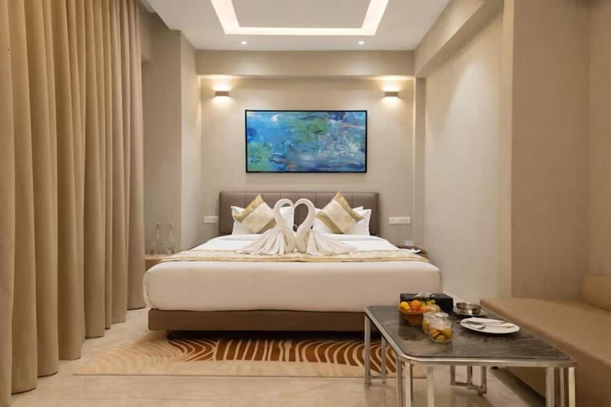 A hotel room with a bed, a painting on the wall, a table with breakfast items, and a sofa.
