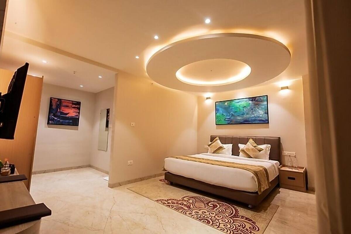 Una habitació d'hotel moderna amb un llit gran, un televisor de pantalla plana, una làmpada de sostre circular i un quadre a la paret.