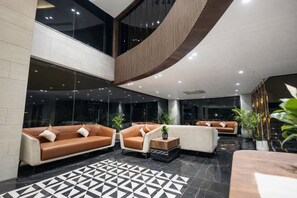 A modern lobby with leather sofas, a geometric patterned floor, and a large glass wall. - Saaz Hotel Indore (Indore)