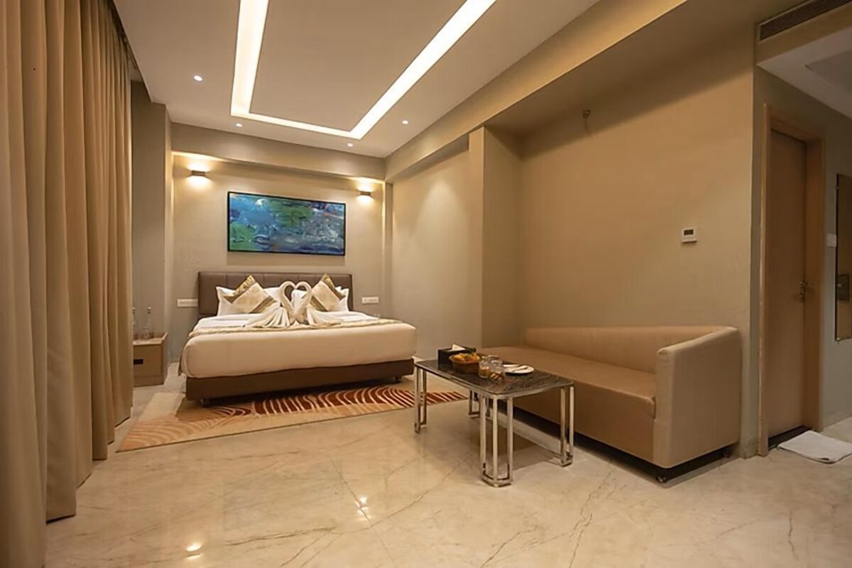 A modern hotel room with a bed, a sofa, a coffee table, and a painting on the wall.