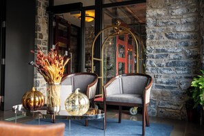 A lobby with a stone wall, a glass door, two chairs, a glass table, and decorative vases. - The British Hotel (Gatineau)