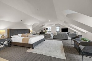 A spacious attic bedroom with a large bed, a sofa, a TV, and a desk. - The British Hotel (Gatineau)