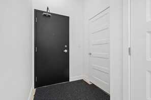 A hallway with a black door, a white door with horizontal handles, and a carpeted floor.