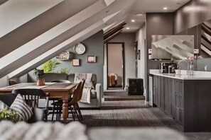 A modern kitchen with a central island, a dining area with a table and chairs, and a staircase leading to an upper level. - The British Hotel (Gatineau)