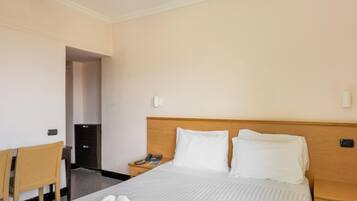 Une chambre d’hôtel équipée d’un lit, d’un bureau, d’une chaise, d’une table de chevet, d’un téléphone et d’un ventilateur de plafond.