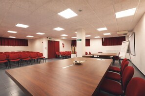 A conference room with a large wooden table, red chairs, a whiteboard, and a projector screen. - Hotiday Bordighera (Bordighera)