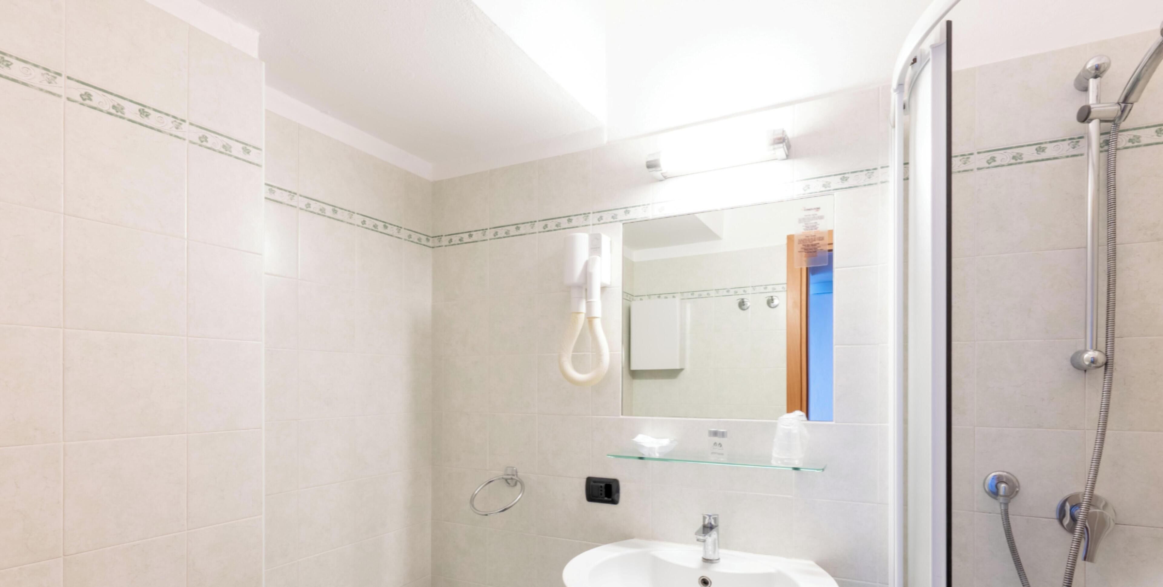 A bathroom with a shower, a sink, a glass shelf, and a mirror.