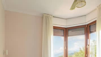 Habitación de hotel con cama, ventilador de techo, ventana con vista y puerta.