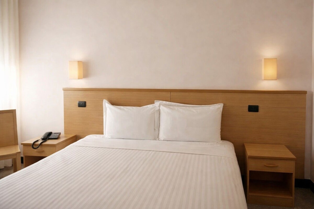 A hotel room with a large bed, two bedside tables, a bedside phone, and two wall-mounted lamps.