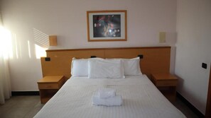 A hotel room with a large bed, two bedside tables, a framed picture on the wall, and a window with blinds. - Hotiday Bordighera (Bordighera)