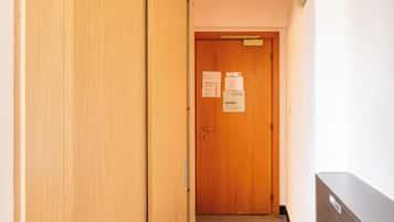 Un pasillo con una puerta de madera al final, un tablón de anuncios y un radiador en la pared.