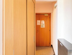 A hallway with a wooden door at the end, a bulletin board with notices, and a radiator on the wall. - Hotiday Bordighera (Bordighera)