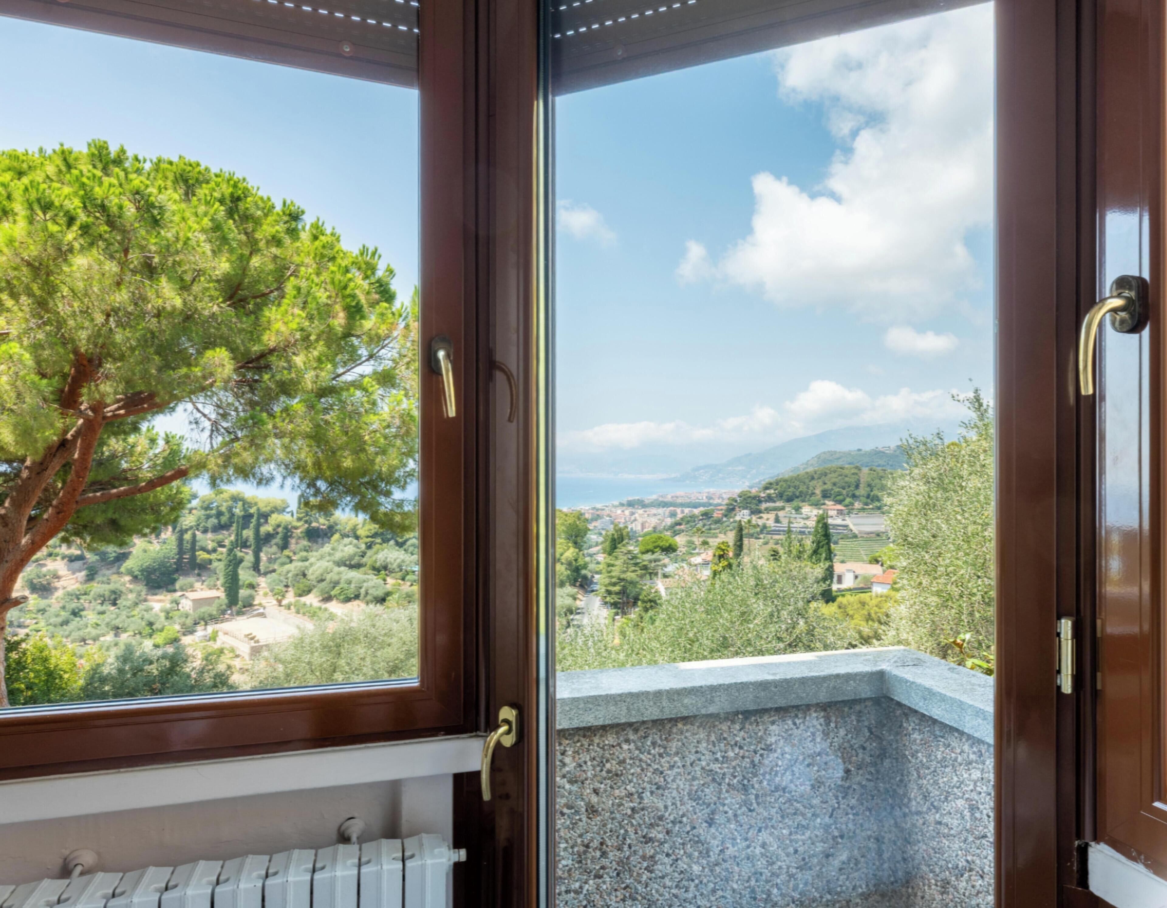 Una habitación con vista a un árbol y un paisaje lejano a través de una ventana.