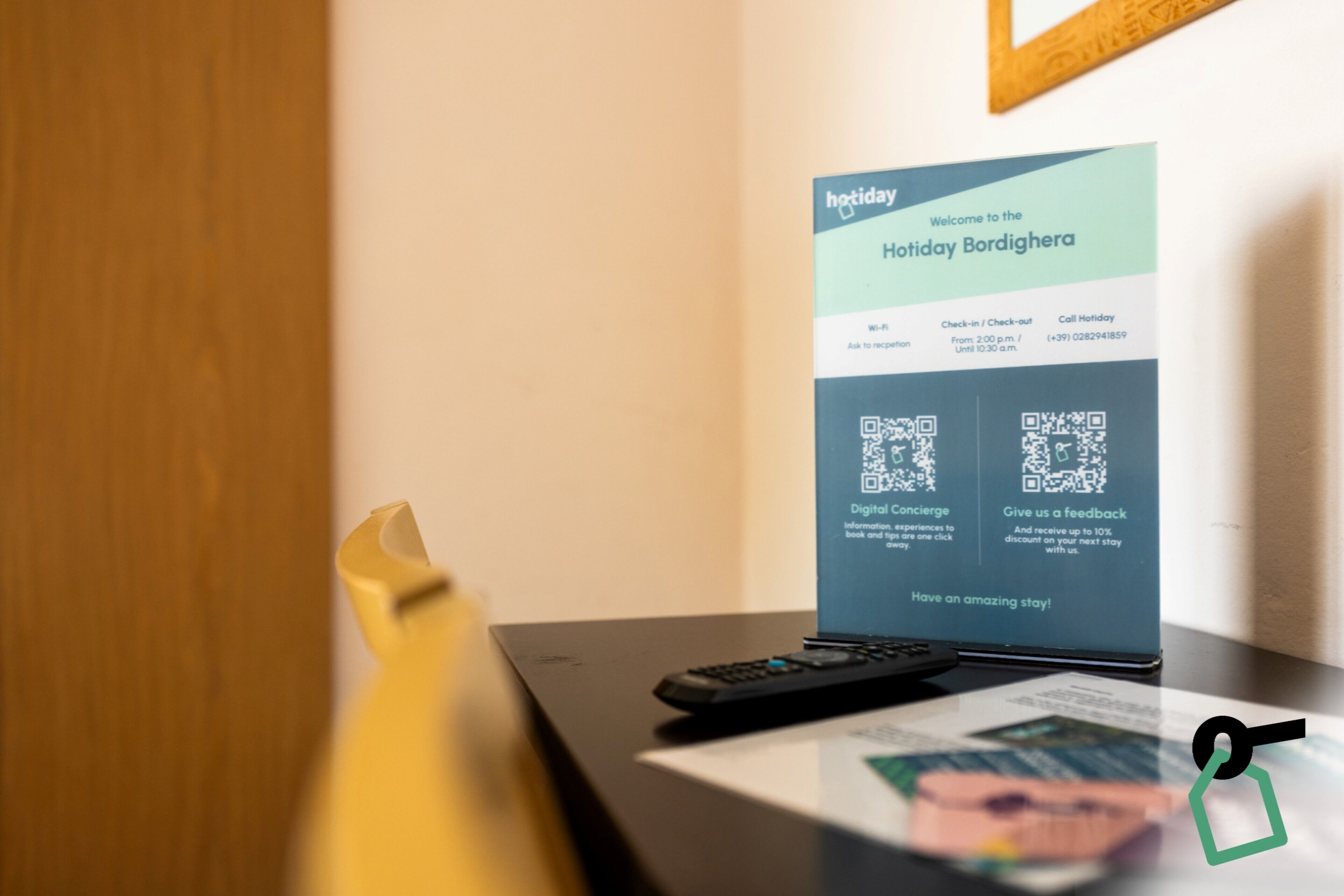 A hotel welcome sign with QR codes for digital concierge and feedback, a remote control, and a yellow object on a table.