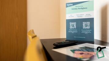 Ein Willkommensschild des Hotels mit QR-Codes für digitalen Concierge-Service und Feedback, einer Fernbedienung und einem gelben Gegenstand auf einem Tisch.