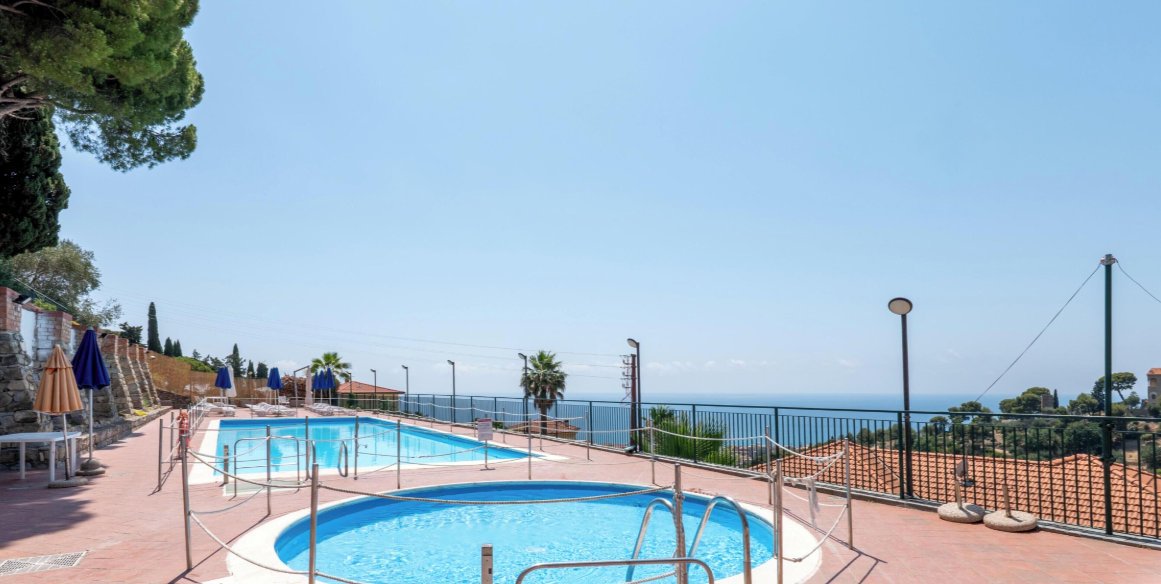 A pool area with two pools, a fence, and a view of the sea.