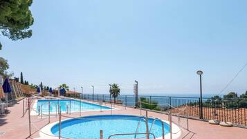 A pool area with two pools, a fence, and a view of the sea.