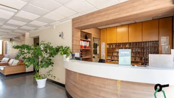 En receptionsdisk med träinredning, en krukväxt, en soffa och en bokhylla med diverse föremål.