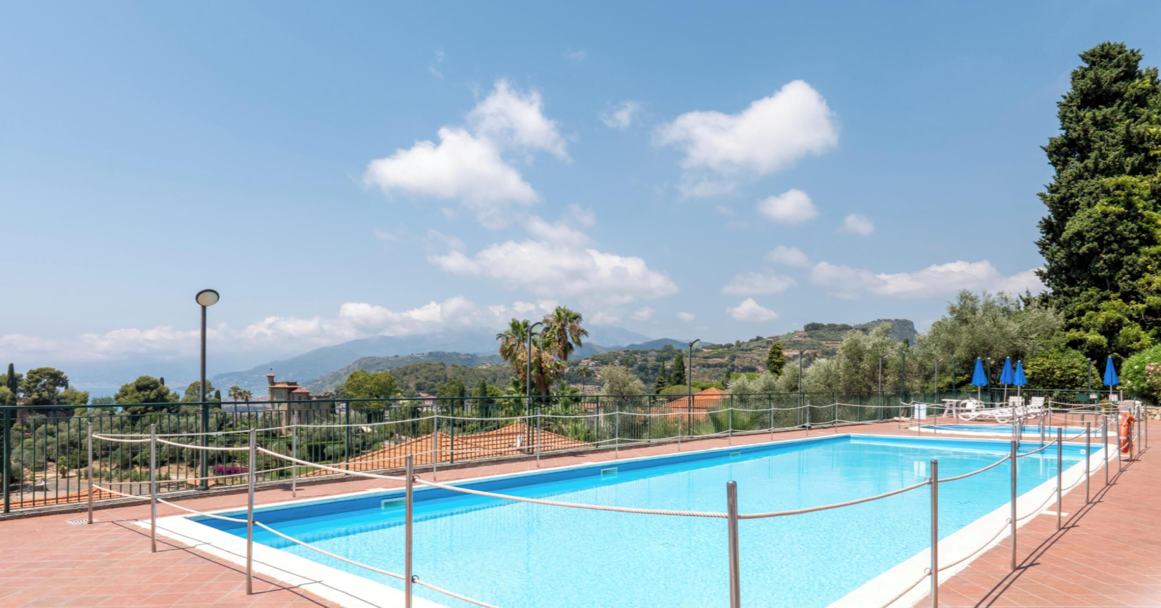 Una piscina rectangular con cielo azul despejado y montañas lejanas al fondo.