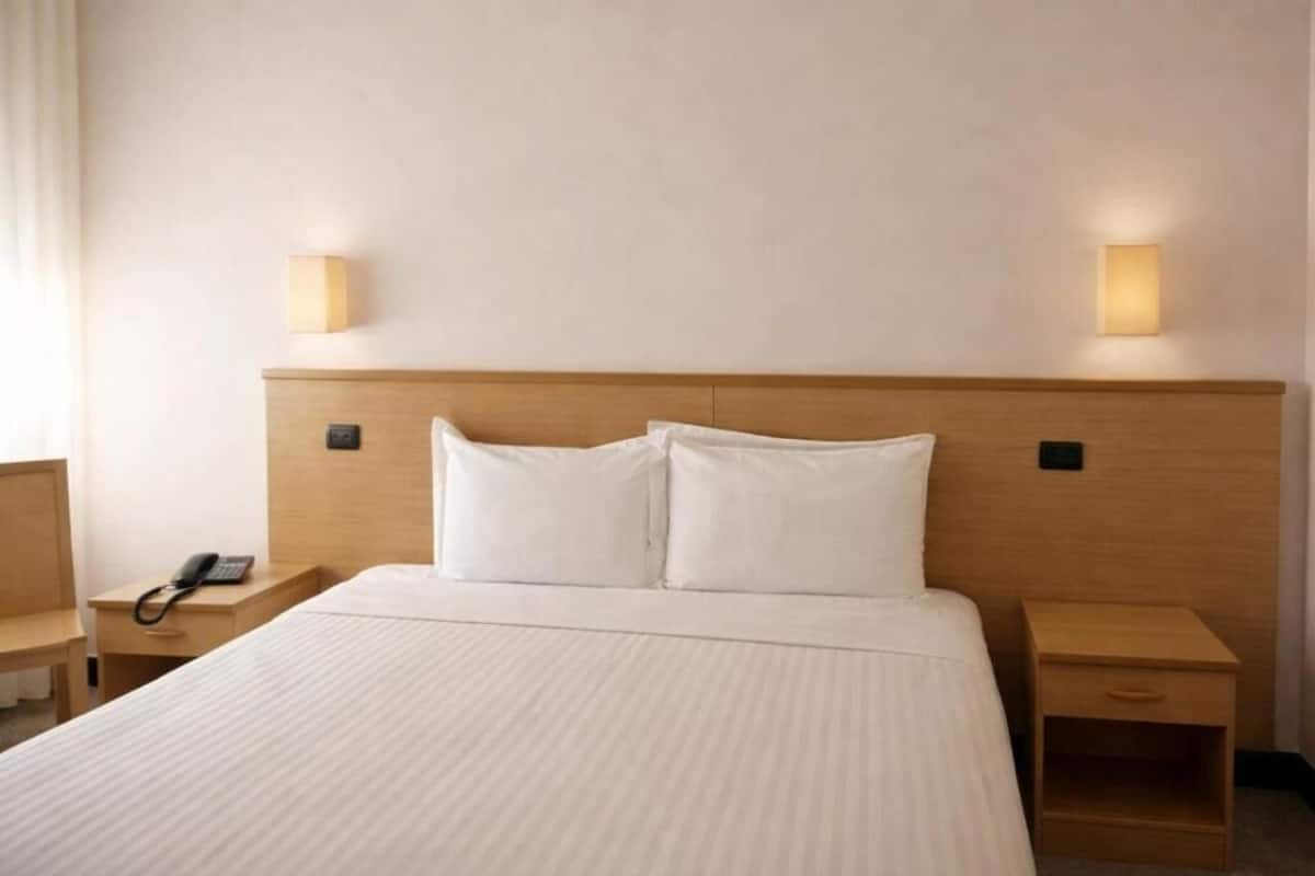 Ett hotellrum med en stor säng, sängbord, en telefon och väggmonterade lampor.