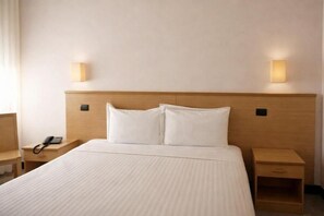 A hotel room with a large bed, bedside tables, a phone, and wall-mounted lights.