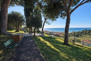 Un sentier qui mène à un banc d’où l’on peut admirer la mer et une ville au loin.