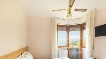 Una habitación de hotel con cama, ventilador de techo, televisor y vistas al exterior.