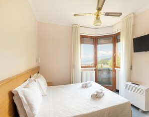 A hotel room with a bed, a ceiling fan, a TV, and a view of the outdoors. - Hotiday Bordighera (Bordighera)