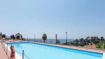 Una piscina con vistas claras al mar y un área vallada con sillas de descanso.