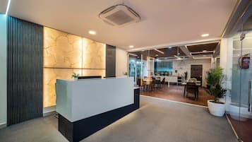 Uma área de recepção com design moderno, com balcão de atendimento, parede estampada e divisória de vidro separando a recepção da sala de jantar.