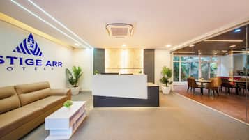 Uma área de recepção de hotel com balcão, sofá, mesa de centro e espaço de refeições com cadeiras e mesa.